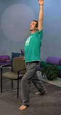 man holding chair while standing in warrior pose reaches up with one arm